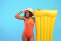 Young black lady in swimsuit with inflatable lilo holding hand above her eyes, looking into distance on blue background Royalty Free Stock Photo