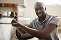 Young black male plumber sitting on the floor fixing a bathroom sink, looking to camera, close up Royalty Free Stock Photo