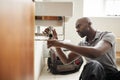 Young black male plumber sitting on the floor fixing a bathroom sink, seen from doorway Royalty Free Stock Photo