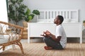 Young black man doing yoga and sitting in lotus position at home