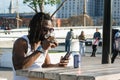 young black man with dreadlocks sitting outdoors at sunset having a cold drink and using the phone