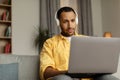 Young black man in headphones using laptop pc, working online, sitting on couch at home, empty space Royalty Free Stock Photo