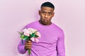 Young black man holding bouquet of white flowers scared and amazed with open mouth for surprise, disbelief face Royalty Free Stock Photo