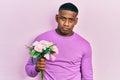 Young black man holding bouquet of white flowers thinking attitude and sober expression looking self confident