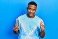 Young black man holding colored pencils smiling happy and positive, thumb up doing excellent and approval sign Royalty Free Stock Photo