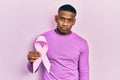 Young black man holding pink cancer ribbon thinking attitude and sober expression looking self confident