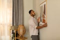 Young black man putting picture frame, hanging painting on wall, empty space. Home interior and domestic decor Royalty Free Stock Photo