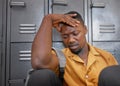 A young black man sits, head in his hand on campus looking upset, stressed