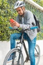 Young black man sitting on a bike in a park, leaning on the handlebars, checking his cell phone