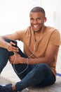 Young black man sitting on ground and listening to music on smart phone