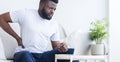 Young black man touching his sore back, working on laptop