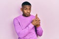 Young black man wearing casual pink sweater holding symbolic gun with hand gesture, playing killing shooting weapons, angry face Royalty Free Stock Photo