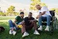 Young Black man in a wheelchair and his male friends taking selfie with phone sitting on the grass together in a park. Royalty Free Stock Photo