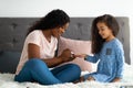 Young black mother applying polish on her adorable daughter& x27;s nails on bed at home, full length Royalty Free Stock Photo