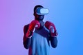 Young black sportsman in VR headset and boxing gloves having virtual workout in neon light