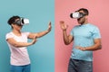 Young black spouses in VR headset touching air during virtual reality experience, blue and pink studio background Royalty Free Stock Photo