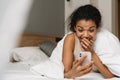 Young black surprised woman using smartphone while lying in bed