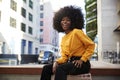 Young African American woman with afro hair sitting on a chair in the street laughing to camera Royalty Free Stock Photo