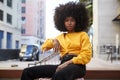 Young African American woman with afro hair and yellow top sitting on a chair in the street looking to camera Royalty Free Stock Photo