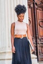 Young black woman with afro hairstyle, wearing sleeveless light color top, black skirt, dark orange belt, holding laptop computer Royalty Free Stock Photo