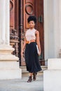 Young black woman with afro hairstyle working in New York, wearing sleeveless light color top, black skirt, belt, strappy sandals Royalty Free Stock Photo