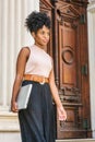 Young black woman with afro hairstyle working in New York, wearing sleeveless light color top, black skirt, dark orange belt, Royalty Free Stock Photo