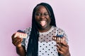 Young black woman with braids holding cheesecakes sticking tongue out happy with funny expression