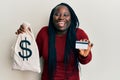 Young black woman with braids holding dollars bag and credit card smiling and laughing hard out loud because funny crazy joke Royalty Free Stock Photo