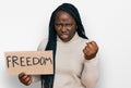 Young black woman with braids holding freedom banner annoyed and frustrated shouting with anger, yelling crazy with anger and hand