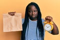 Young black woman with braids holding take away food and alarm clock depressed and worry for distress, crying angry and afraid Royalty Free Stock Photo