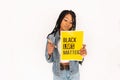 Young black woman with dreadlocks shows yellow poster for protests with text to protect black people.