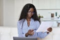 Young black woman holding paper working on laptop at home office. Royalty Free Stock Photo