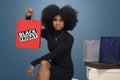 Young black woman holding shopping bag, several boxes and shopping bags beside her