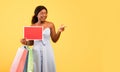 Young black woman holding shopping bags and empty sign with mockup, pointing at blank space over orange background Royalty Free Stock Photo