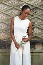 Young black woman holding white rose, standing outdoors in New York City, looking down, thinking Royalty Free Stock Photo