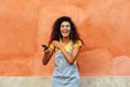 Young black woman laughing and listening to music with earphones outdoors. Arab girl in casual clothes with curly hairstyle in Royalty Free Stock Photo