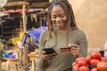 young black woman selling in a local african market using her mobile phone and credit card to do a transaction online smiling Royalty Free Stock Photo