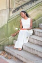 Young black woman sitting on stairs with red book and white rose flowers in New York City, thinking Royalty Free Stock Photo