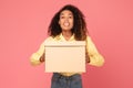 Young black woman smiles holding parcel on pink backdrop Royalty Free Stock Photo