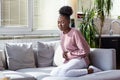 Young black woman suffering from stomachache on sofa at home. Woman sitting on bed and having stomach ache. Young woman suffering Royalty Free Stock Photo