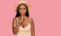 Young black woman wearing summer hat asking to be quiet with finger on lips Royalty Free Stock Photo