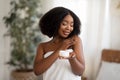 Young black woman wrapped in towel applying body lotion or cream after shower at home Royalty Free Stock Photo