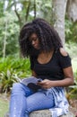 A young black woman between 20 and 30 years old sitting reading a book alone, in a park Royalty Free Stock Photo