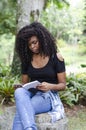 A young black woman between 20 and 30 years old sitting reading a book alone, in a park Royalty Free Stock Photo