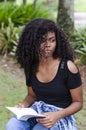 A young black woman between 20 and 30 years old sitting reading a book alone, in a park Royalty Free Stock Photo