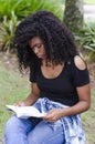 A young black woman between 20 and 30 years old sitting reading a book alone, in a park Royalty Free Stock Photo