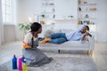 Young black woman sitting on floor, cleaning apartment, arguing with her idle husband over domestic duties Royalty Free Stock Photo