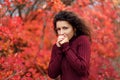 Young blackhaired woman in red sweather heating her hands by blowing stay in red autumnn bushes