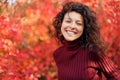 Young blackhaired woman in red sweather posing on camera in red autumnn bushes