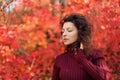 Young blackhaired woman in red sweather posing on camera in red autumnn bushes